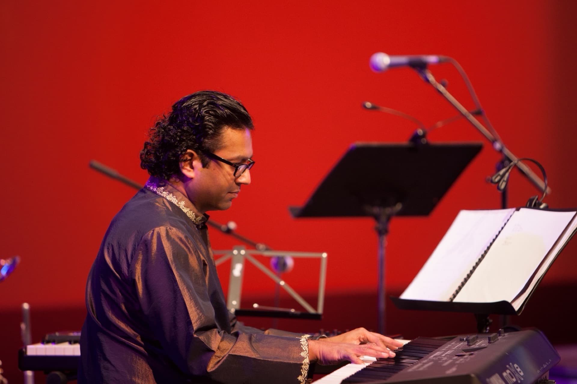 Ben Fernandez performing at a stage keyboard against a red backdrop.
