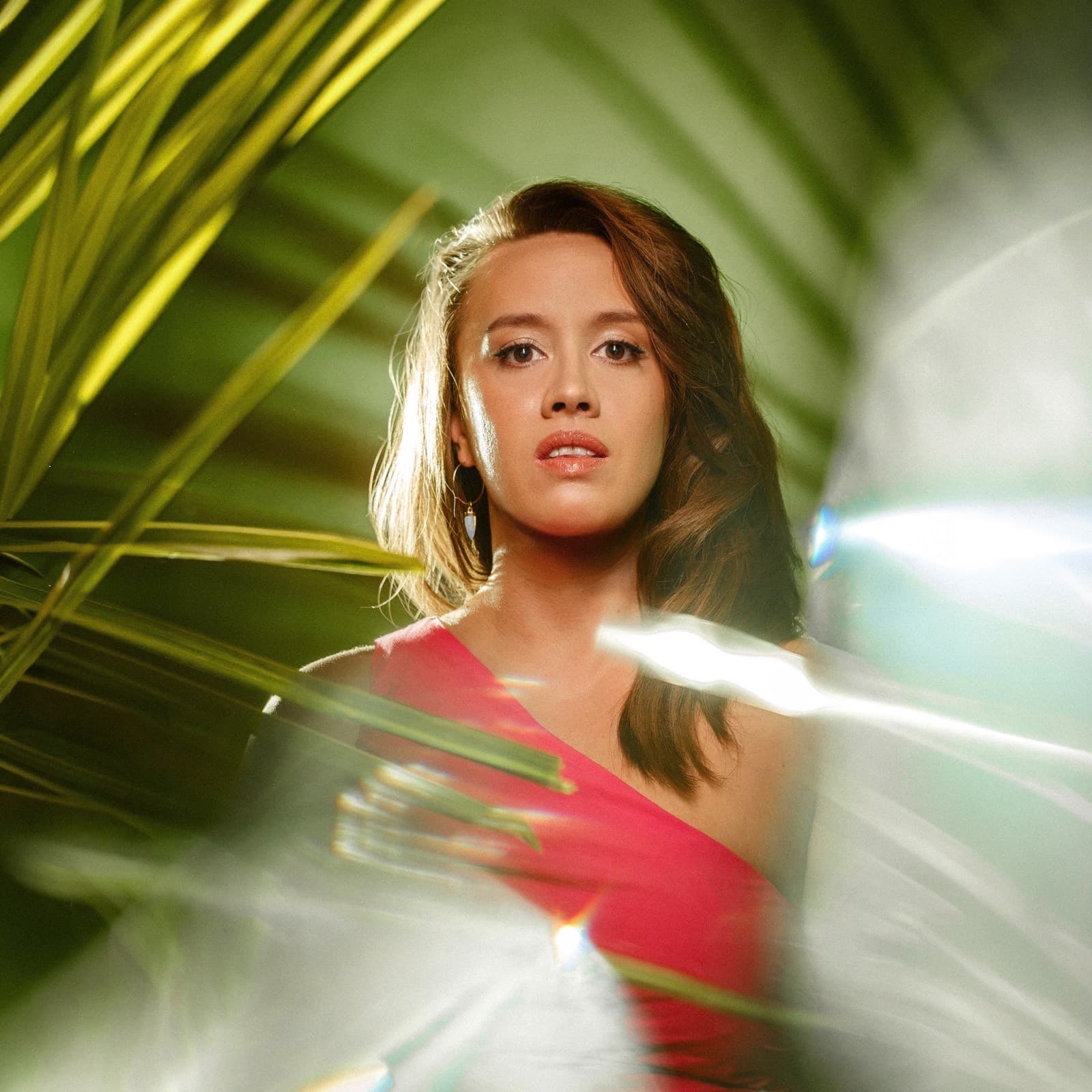 Rā Charmian in a magenta top against tropical foliage and soft stage light.